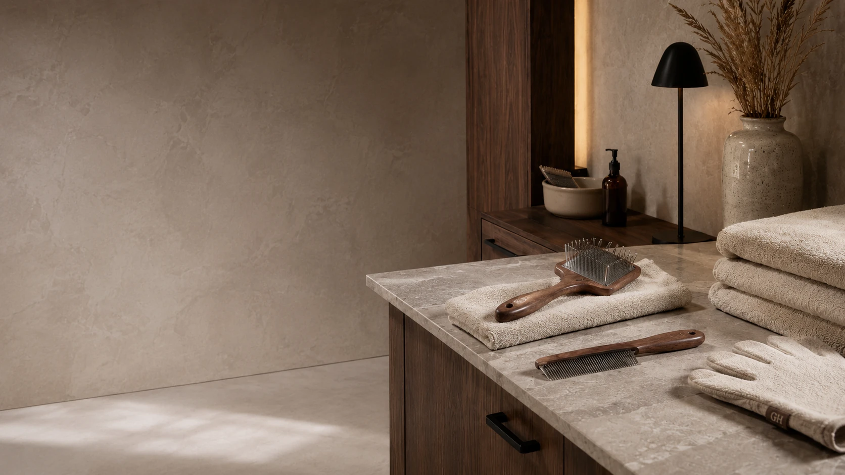 Rincón de cuidado en vivienda moderna premium: cepillo de mango de madera, carda, toalla plegable y botes sobre mueble de nogal y piedra; cuidado diario y sereno